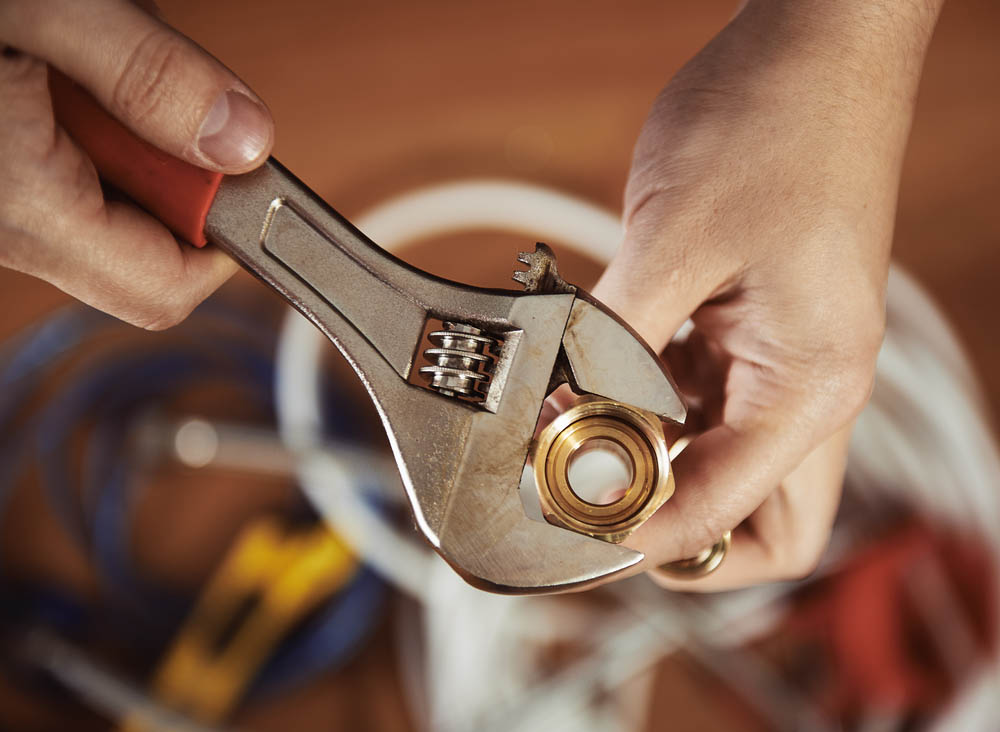Close-up of plumber hands screwing nut of pipe with wrench over plumbing tools background.  Concept of repair and technical assistance.