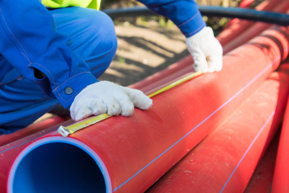 builder's hands in white gloves, measure the length of the red plastic pipe, yellow tape measure, to mark the size, close-up